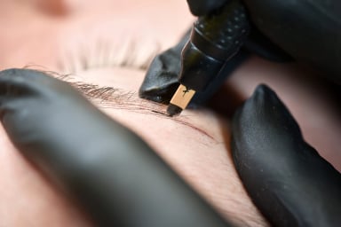 Close-up of eyebrow microblading procedure with a pen.