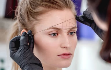 A woman getting her eyebrows shaped by threading.